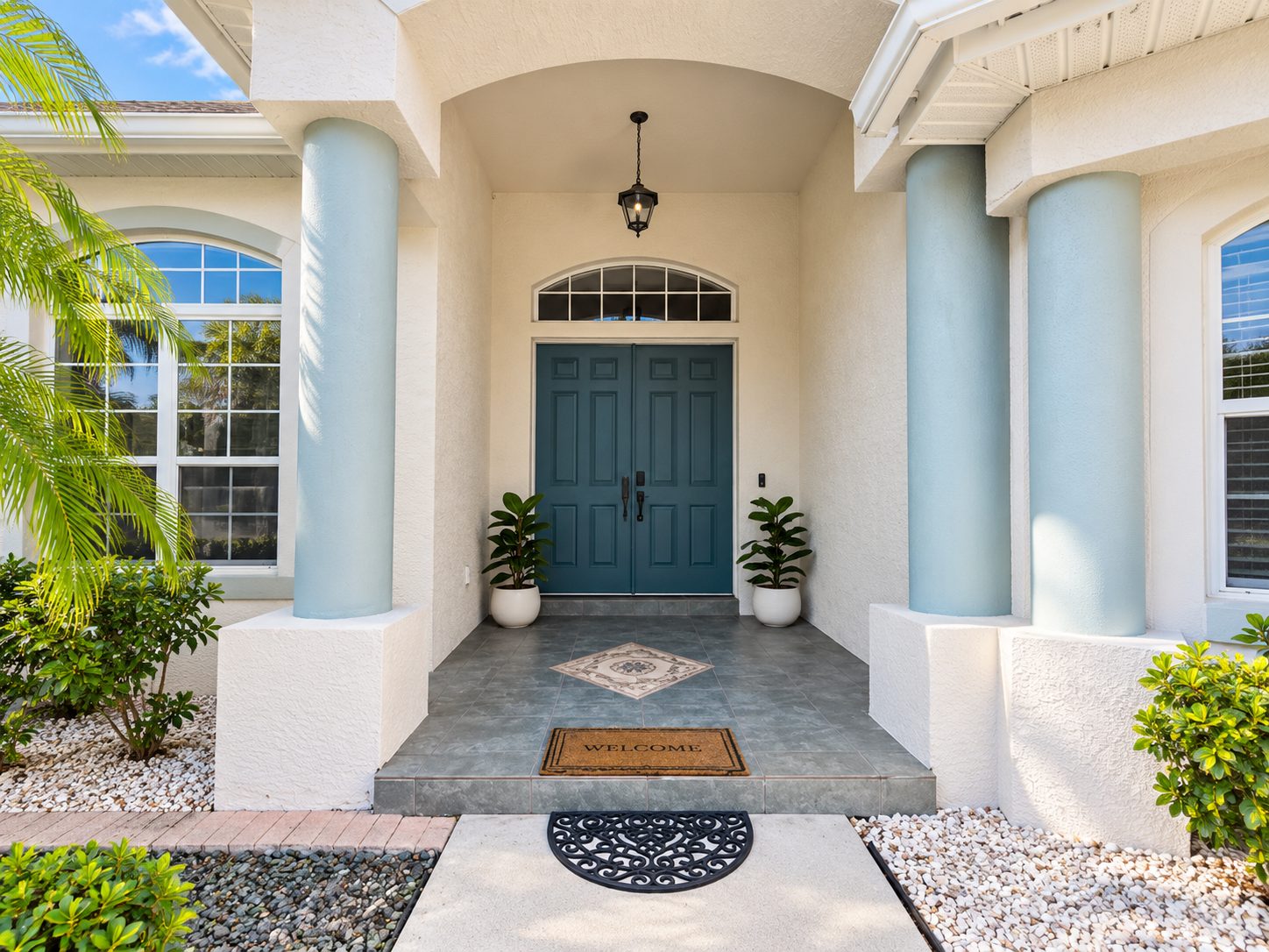Teal double front doors under an arched covered porch with white columns and potted plants at the Nokomis Beach House.