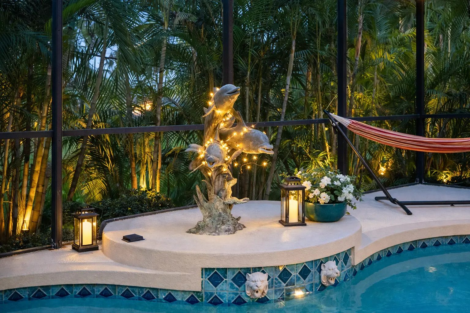 An evening view of the screened pool area with a dolphin sculpture, lanterns and hammock.